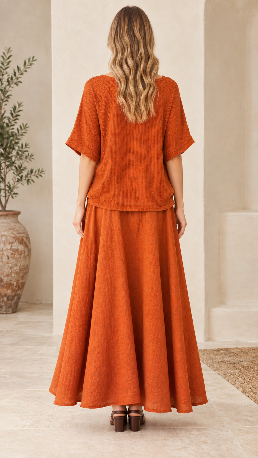 Back full-length view of woman in rust orange matching top and long skirt set