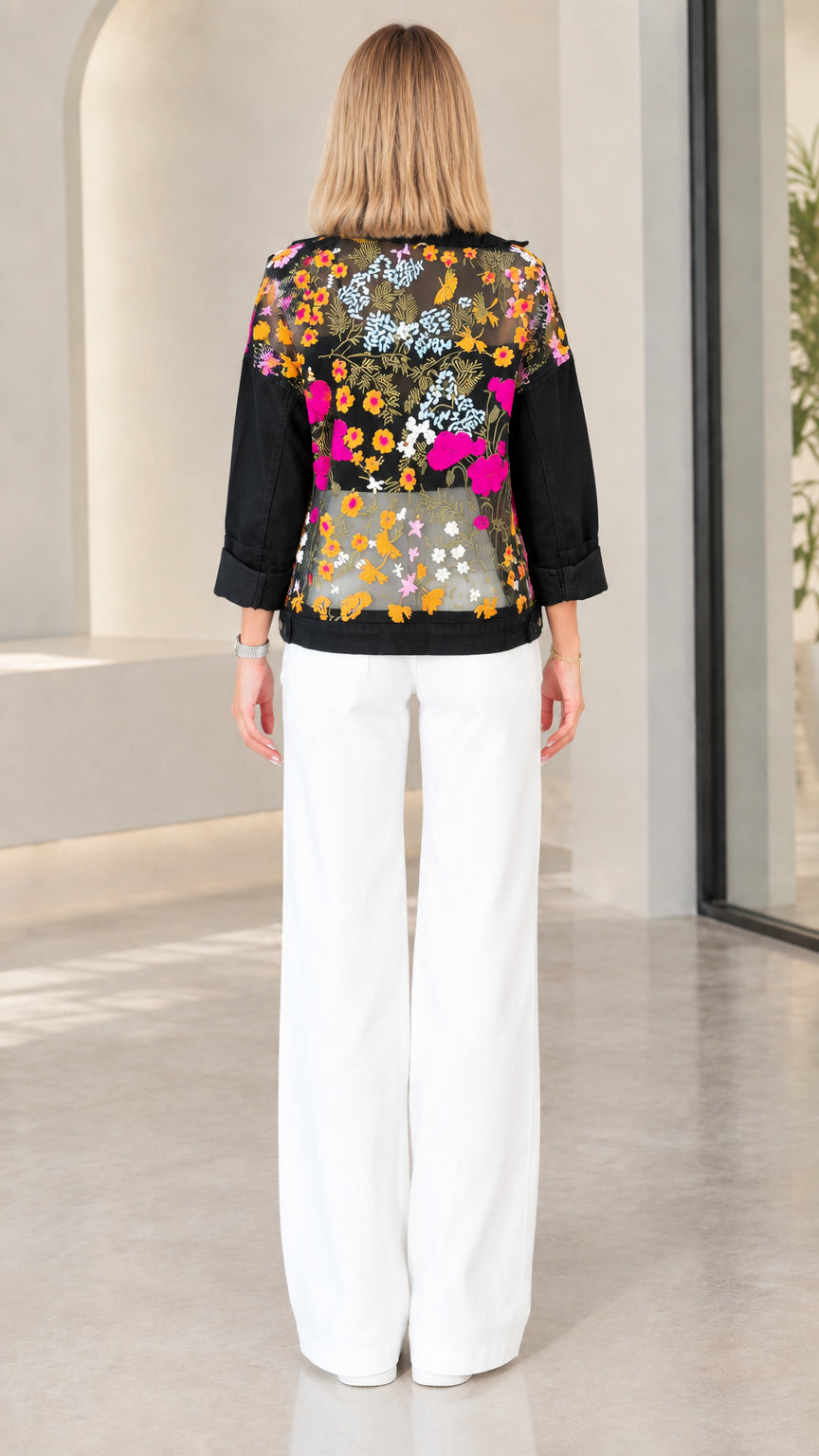 Back view of model showing full floral embroidery on sheer mesh back panel of black jacket