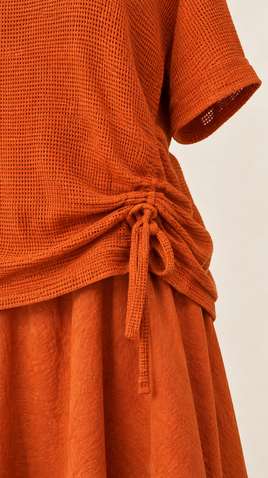 Close-up detail of textured knit fabric and side drawstring tie on rust top