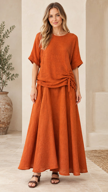 Front full-length view of woman wearing rust orange textured short sleeve top and matching maxi skirt set