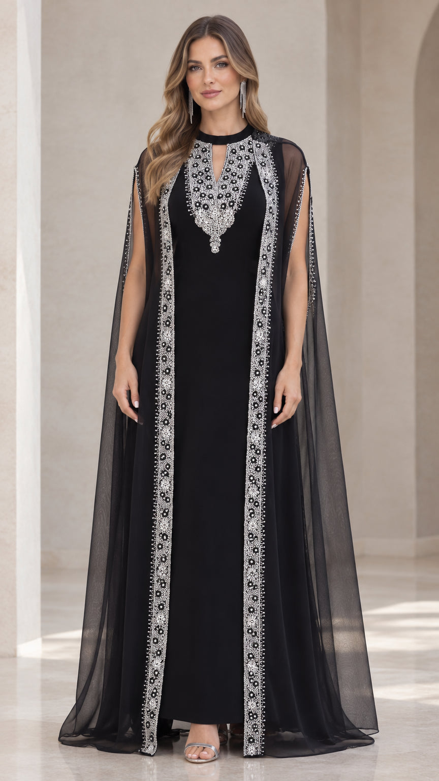 Front full view of black embellished cape evening gown with sheer overlay