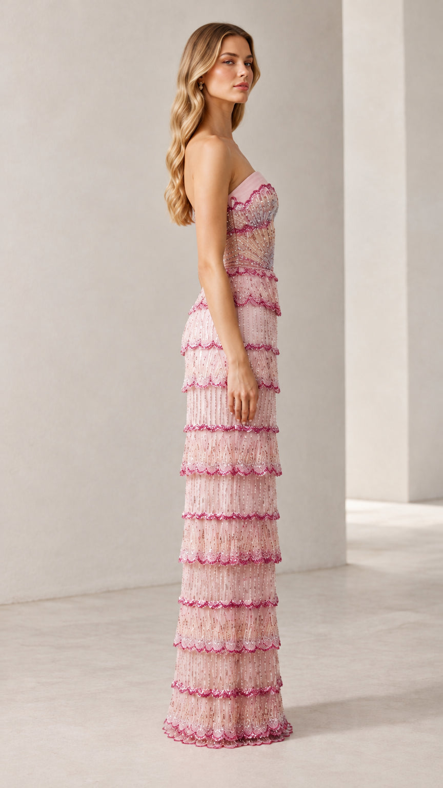 Side profile view of woman wearing strapless blush pink beaded tiered maxi gown