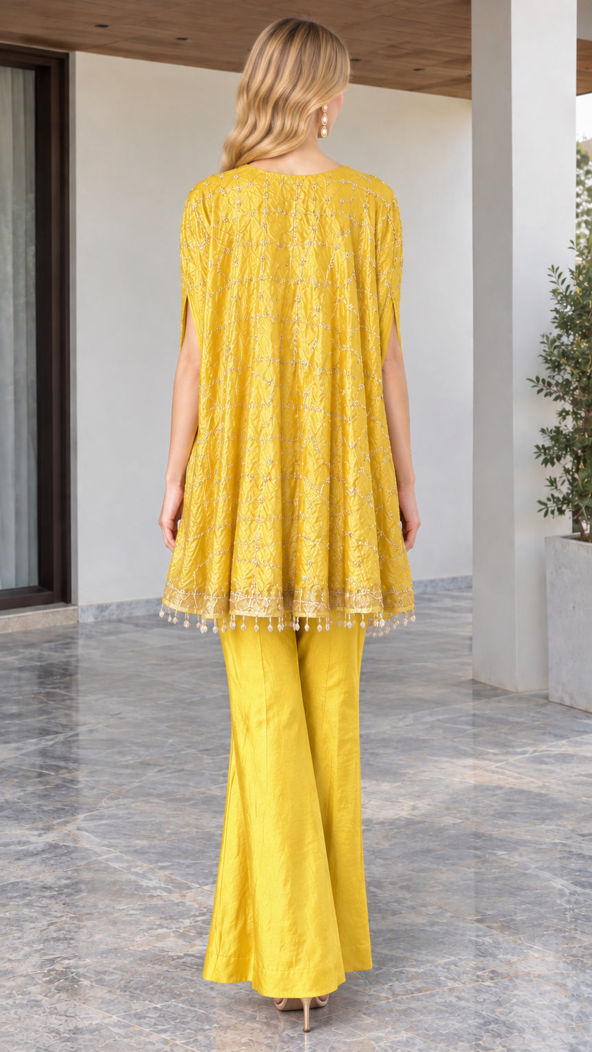 Back view of model in yellow cape-sleeve embroidered tunic and flare pants