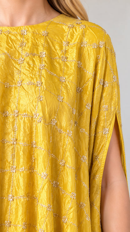 Close-up detail of textured yellow fabric with delicate embroidery and beaded fringe