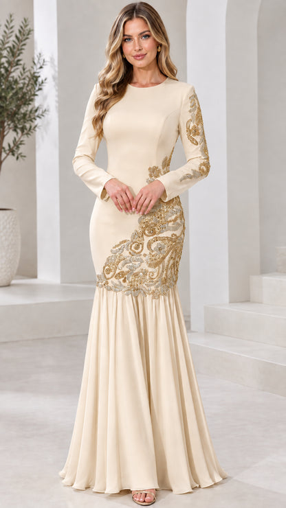 Model wearing champagne cream long sleeve mermaid gown with gold embroidery